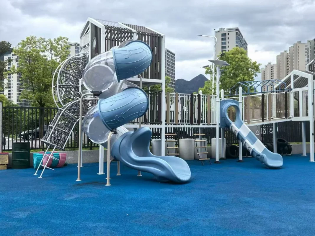 Playground Equipment Manufacturer | Indoor Soft Play & Custom Outdoor Playgrounds | Xinjiu Contemporary outdoor play towers with curved blue tube slides and a climbing net