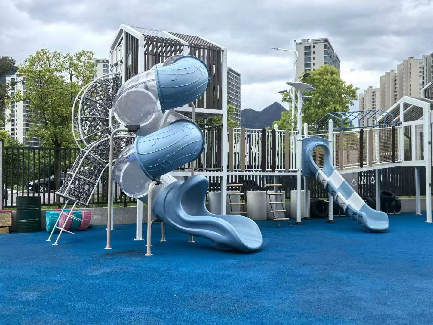 Contemporary outdoor play towers with curved blue tube slides and a climbing net